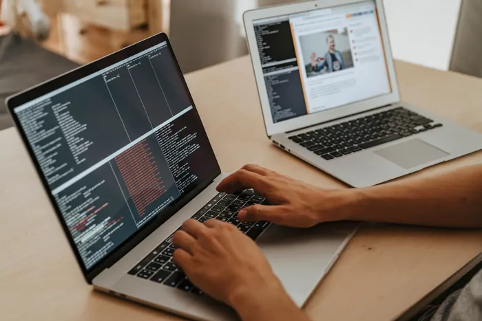 Hands writing code on two laptops